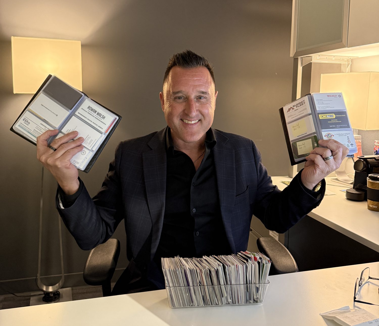 Chris Post of River City Events holding up two binders of business cards, with a basket full of more cards on the desk in front of him
